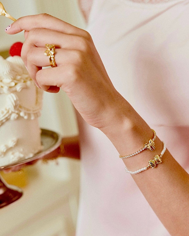 Hand with gold ring and bracelet near a cake
