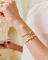 Close-up of a wrist wearing two gold bracelets with floral designs, against a blurred background.