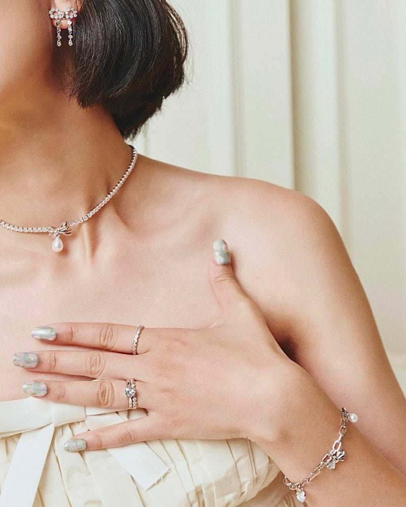 Close-up of a person wearing pearl jewelry including earrings, necklace, ring, and bracelet.